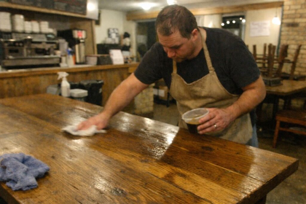 an illustrative image eof a worker re-oiling a large wooden table