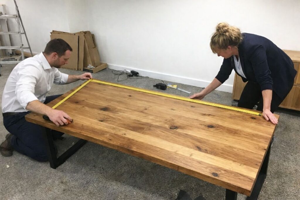 An illustrative image of people measuring and arranging a wooden desk in an office space