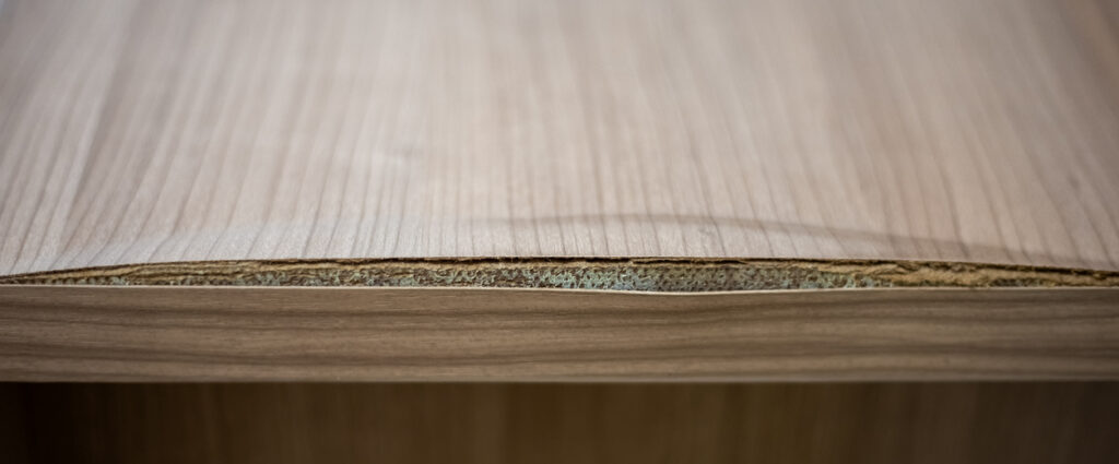Chipped veneer on a table edge showing the board core underneath